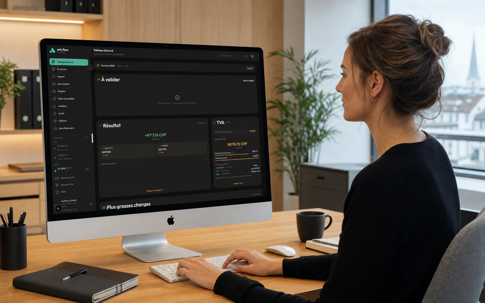 Une professionnelle consulte ark.flow Compta sur un grand iMac dans un bureau suisse lumineux.